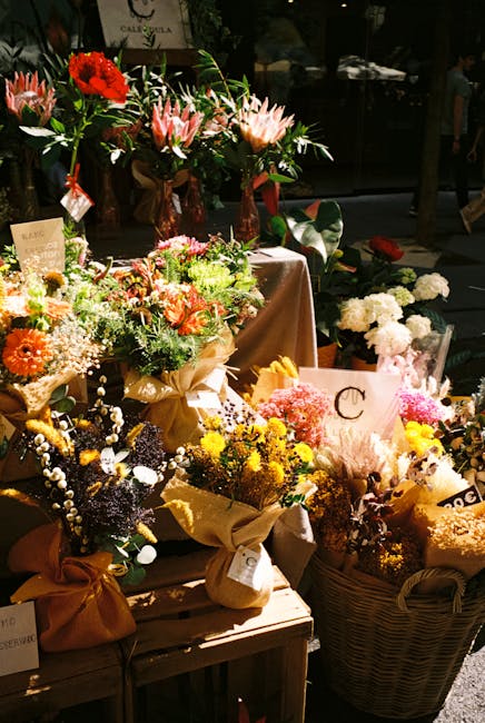 A display of various fresh floral arrangements and bouquets featuring a diverse range of flowers including pink lilies, red roses, yellow chrysanthemums, white and purple asters, and baby's breath, al