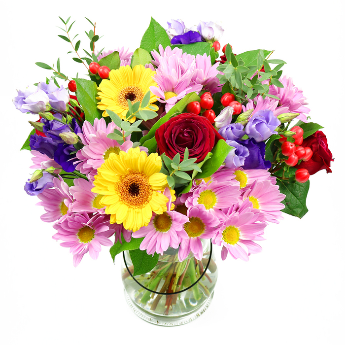 A vibrant, generously filled bouquet stands upright in a clear glass vase, set against a bright white backdrop that throws every flower and leaf into crisp relief. At the centre, deep red roses gather in a cluster of rich, velvety blooms, their tightly layered petals lending an air of classic romance and understated luxury. Surrounding them, golden yellow gerbera daisies with dark brown-orange centres offer bold, open faces that seem to smile, bringing warmth and optimism to the design. Encircling the focal blooms, an abundance of pink daisies or chrysanthemums creates a softly textured halo, their numerous fine petals and tiny yellow centres adding lightness, volume, and a gentle, almost feathery quality. Woven through this pastel ring are elegant lisianthus flowers in shades of purple and lavender, their bell-shaped blooms and slender buds adding both height and a sophisticated, cool note. Tucked among the flowers, rounded red hypericum berries contribute bright, glossy dots of colour, giving the arrangement a playful, contemporary edge and an intriguing texture. Lush green foliage in various tones supports and frames the blooms, with broader dark leaves grounding the composition and lighter, more delicate sprigs reaching outward, softening the silhouette and evoking natural movement. The clear glass vase reveals a fan of neatly cut stems resting in fresh water, a quiet testament to careful, professional preparation. The overall impression is joyful, refined, and welcoming, perfectly suited to brighten a Barbican apartment's minimalist interior, bring life to a desk in an EC1 or EC2 office, or serve as an uplifting gift for a concert performer or theatre lover visiting the nearby Barbican Centre. This bouquet reflects the area's blend of modern architecture, culture, and community warmth.
